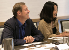 A white man and east asian woman sit side-by-side at a table 