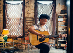 A young black woman playing the guitar.