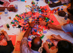 Many hands reaching for several lego pieces on a table