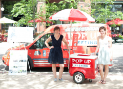 Two white women standing with a popsicle stand that reads "pop up meeting"