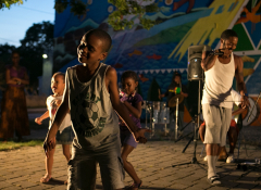 A young black boy dancing in a crowd of three. 