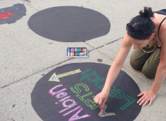 A young woman doing a chalk drawing on the side walk