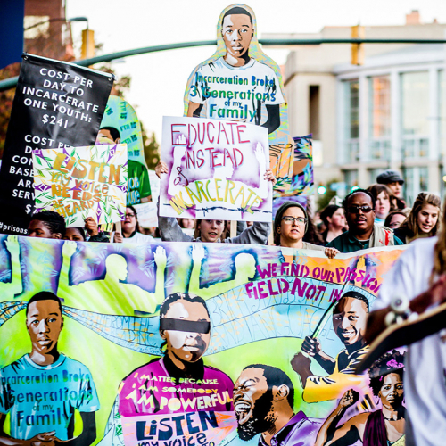 Image of a group of protestors with bright signs featuring black youth