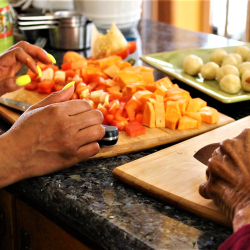 Two pairs of hands cutting vegetables. 