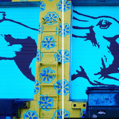 A bright blue mural of a rabbit on a brick wall