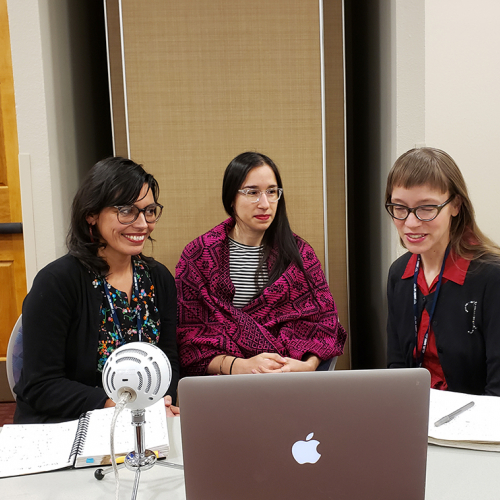 Three women sit by a laptop computer. 