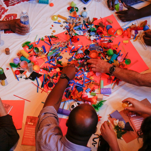Many hands reaching for several lego pieces on a table