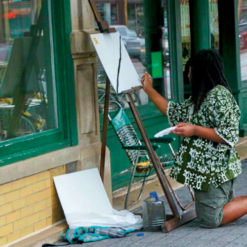 A black artists paints with an easel and canvas on an empty street