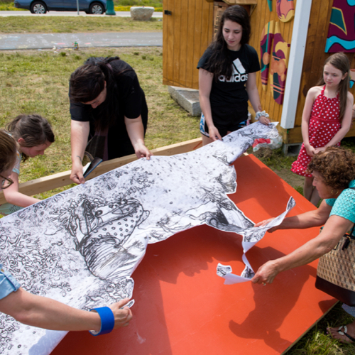 Community members collaborate on the installation of a wheat paste mural depicting a child and elder gardening together.