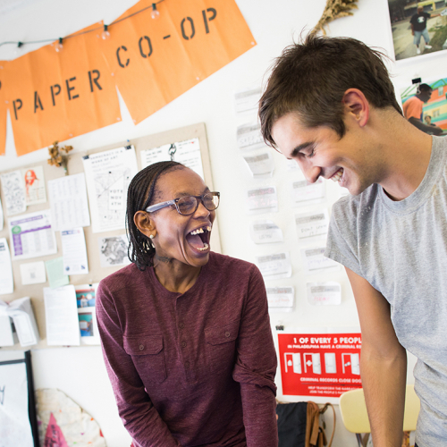 A black woman and a white man smiling and working at the People's Paper co-op 