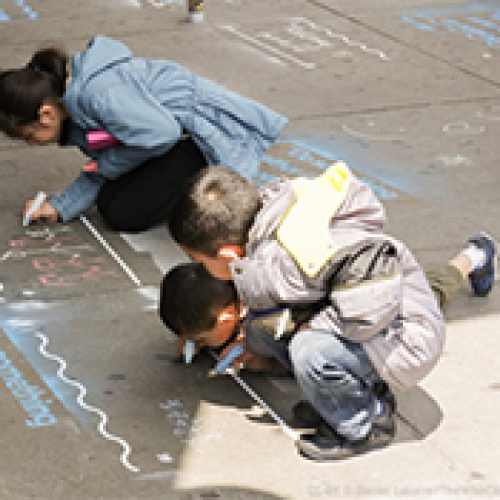Three young kids drawing on the sidewalk with chalk