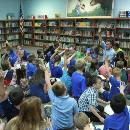 A man speaking to a group of kids in a library