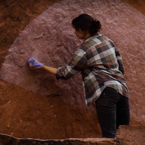 A Native woman painting a semi-circle on a mountain wall