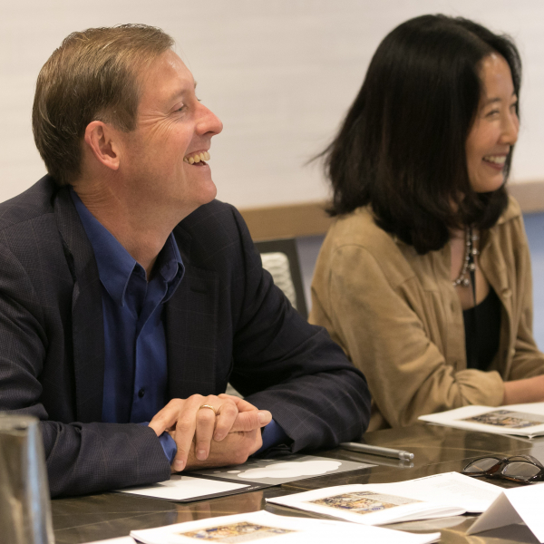 A white man and east asian woman sit side-by-side at a table 