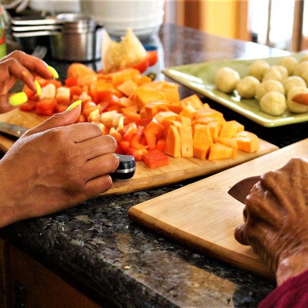 Two pairs of hands cutting vegetables. 