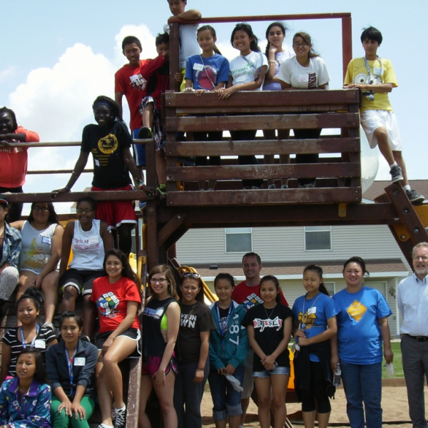 A large group of teens and adults posing around a wooden structure