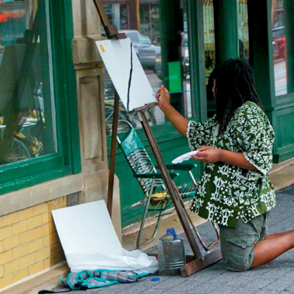 A black artists paints with an easel and canvas on an empty street