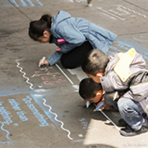 Three young kids drawing on the sidewalk with chalk