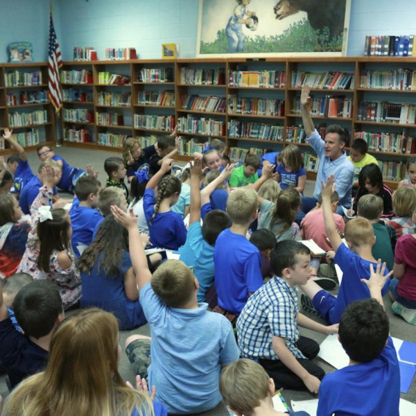 A man speaking to a group of kids in a library