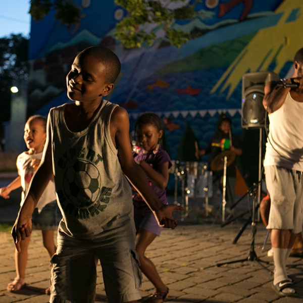 A young black boy dancing in a crowd of three. 